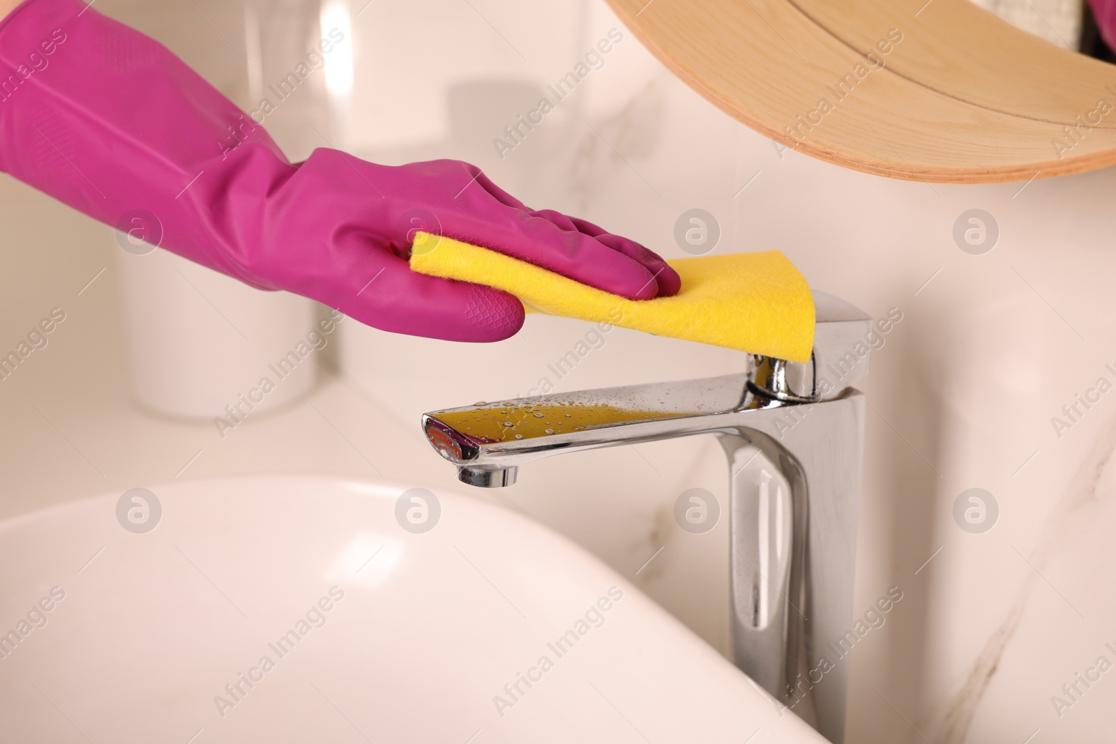 Photo of Woman in gloves cleaning faucet of bathroom sink with rag, closeup