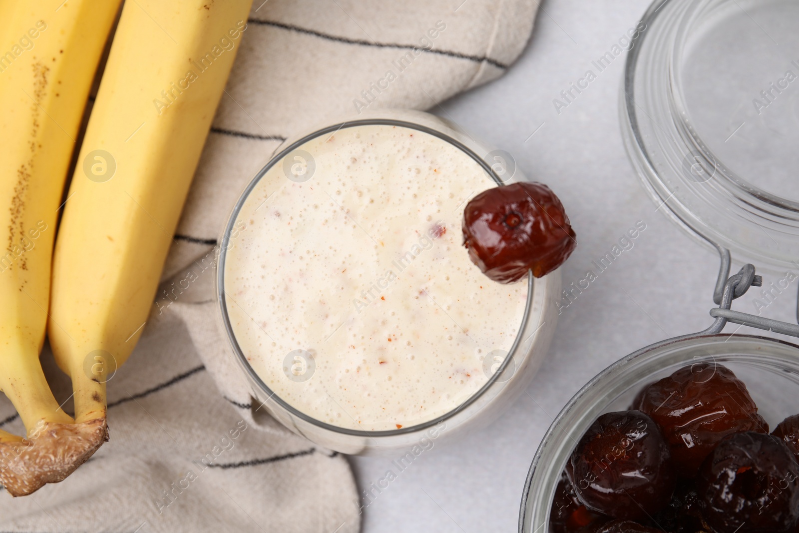 Photo of Glass of delicious date smoothie with mint, dried fruits and bananas on light grey table, flat lay