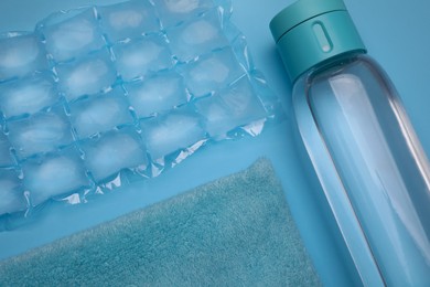 Bottle of water, ice pack and towel on light blue background, flat lay. Heat stroke treatment