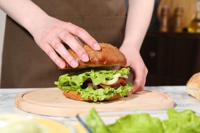 Photo of Woman making delicious vegetarian burger at white marble table, closeup