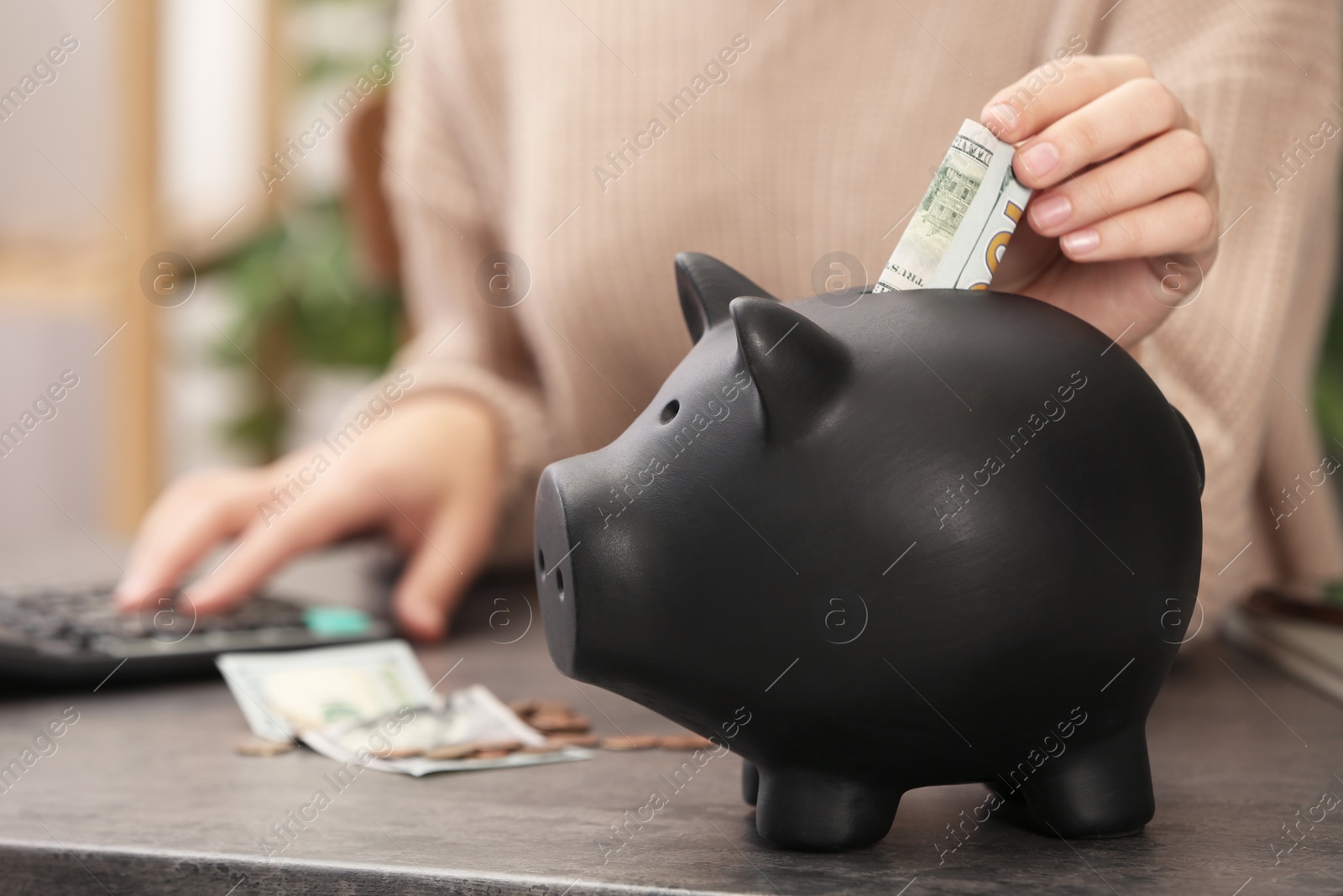 Photo of Woman putting money into piggy bank at table indoors, closeup