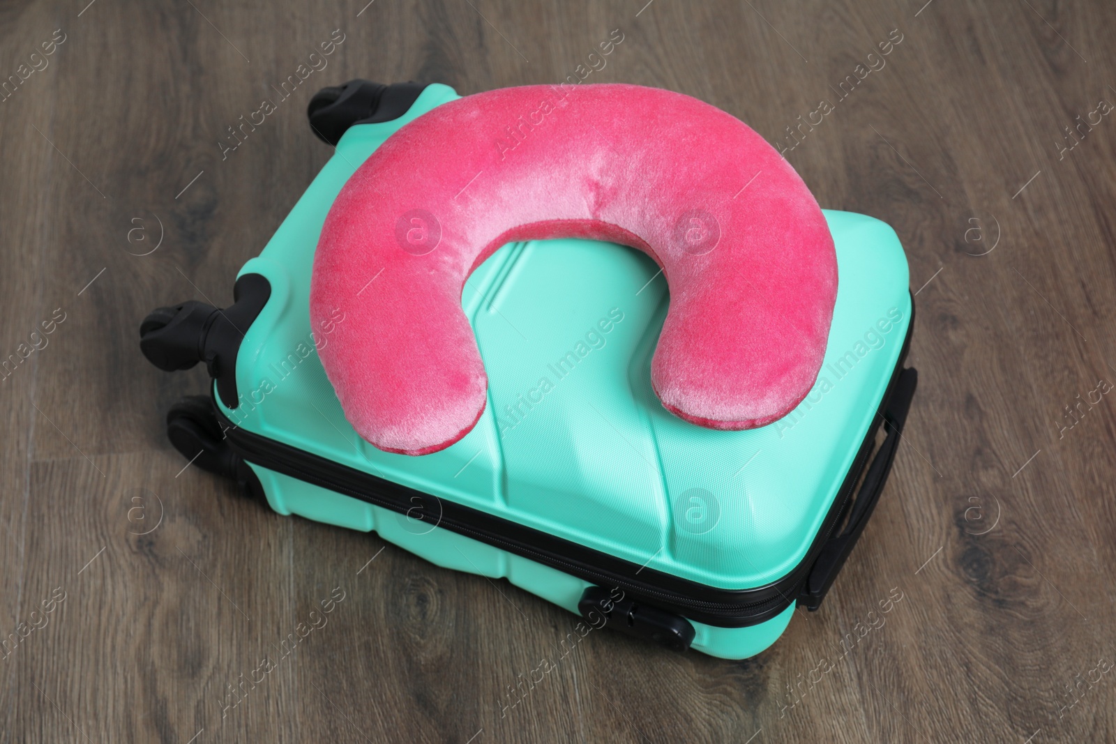 Photo of Pink travel pillow and turquoise suitcase on floor