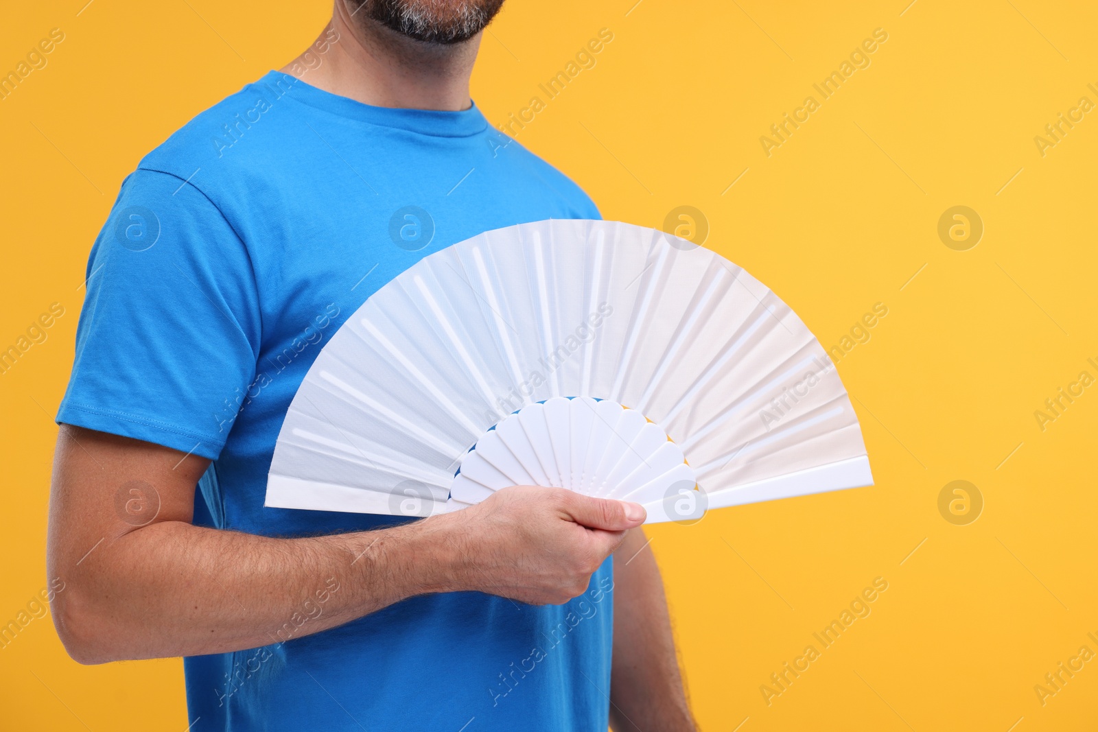 Photo of Man holding hand fan on orange background, closeup