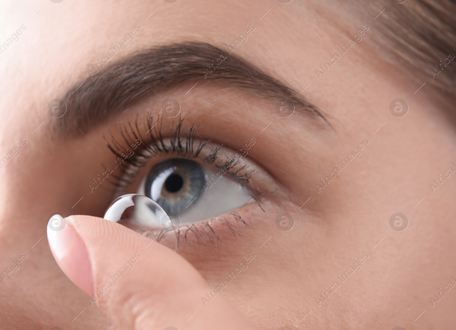 Photo of Young woman putting contact lens in her eye, closeup