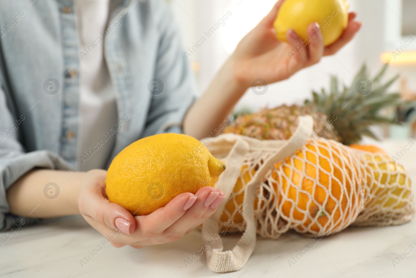 Photo of Woman with lemons and string bag of fresh fruits at light table, closeup