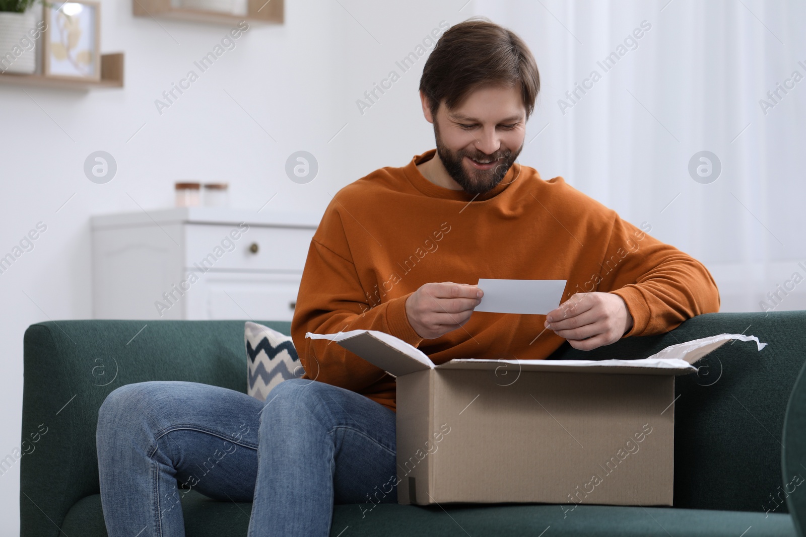 Photo of Happy man with greeting card near parcel at home. Internet shopping