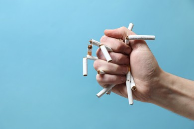 Photo of Stop smoking. Man holding broken cigarettes on light blue background, closeup. Space for text