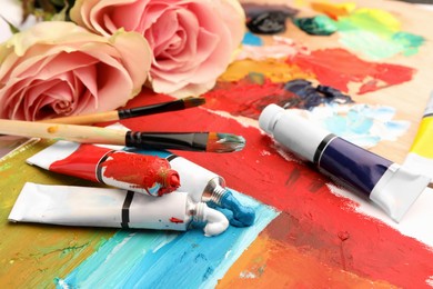 Photo of Tubes of colorful oil paints, flowers and brushes on canvas with abstract painting