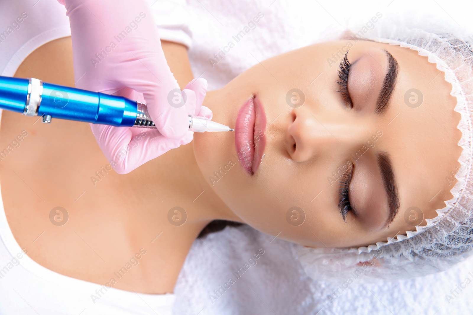 Photo of Young woman getting permanent makeup on lips in beautician salon, closeup