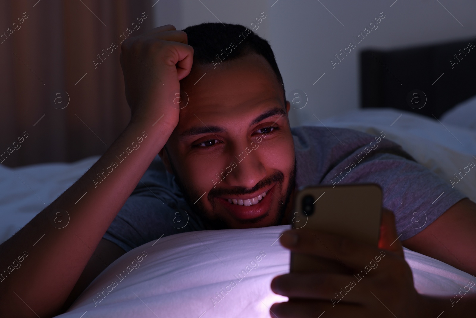 Photo of Happy man using smartphone in bed at night. Internet addiction