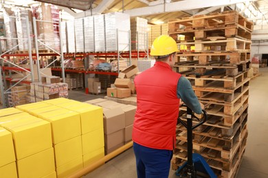 Worker moving wooden pallets with manual forklift in warehouse, back view