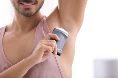 Photo of Handsome young man applying deodorant in room