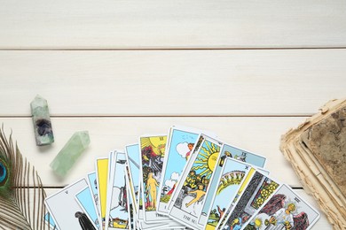 Tarot cards, old book, crystals and peacock feather on white wooden table, flat lay. Space for text