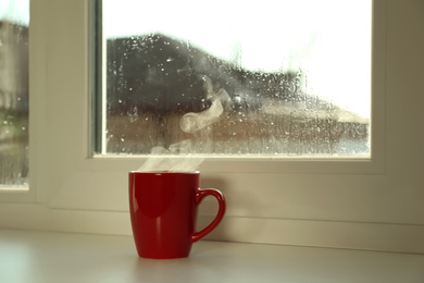 Cup of hot drink near window on rainy day. Space for text