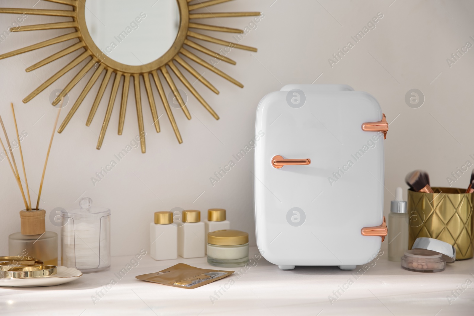 Photo of Cosmetics refrigerator and skin care products on white vanity table indoors