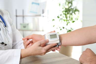 Photo of Doctor checking man's pulse with medical device in hospital, closeup