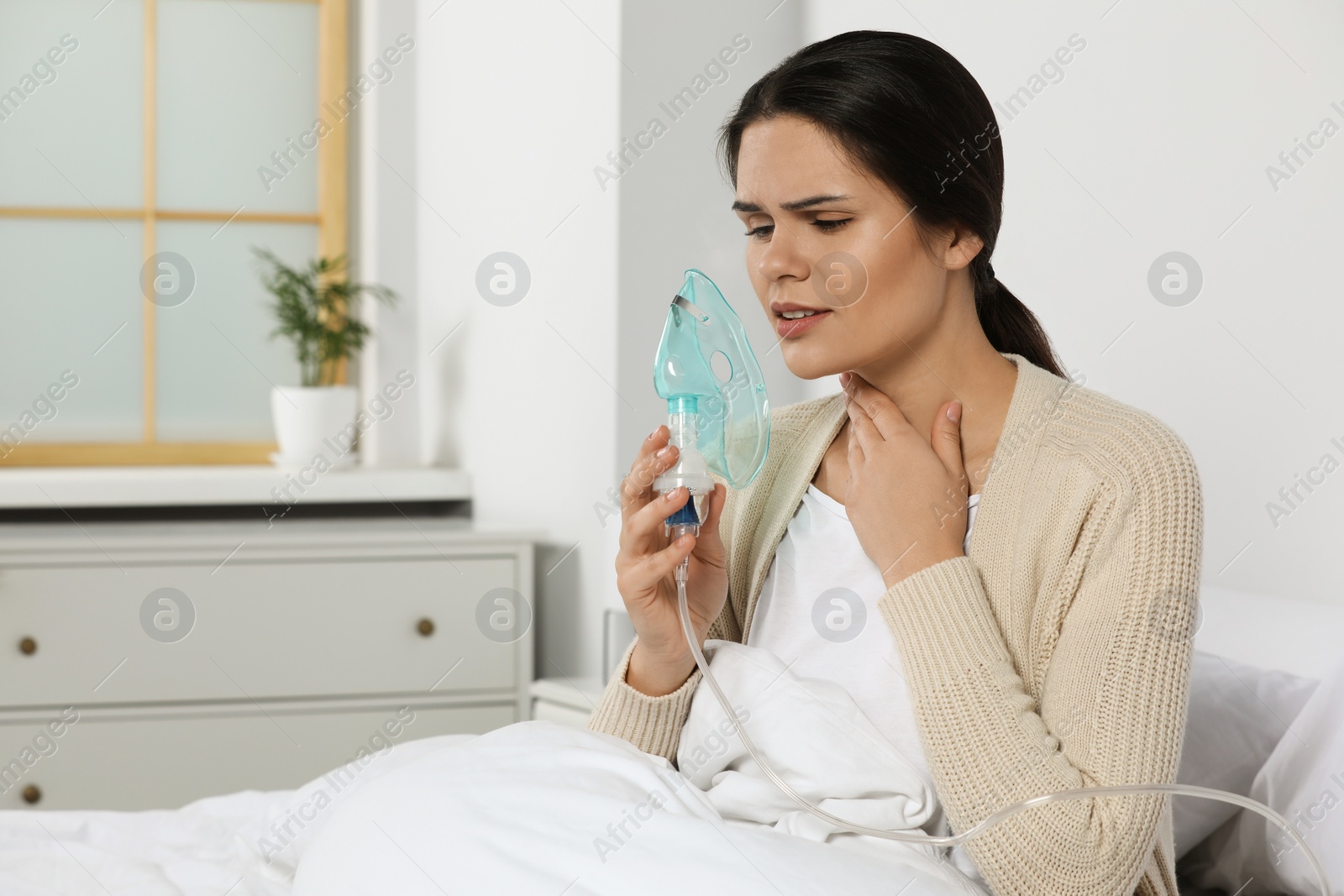 Photo of Sick young woman using nebulizer on bed at home, space for text