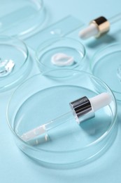 Photo of Petri dishes with cosmetic serums and pipettes on light blue background, closeup