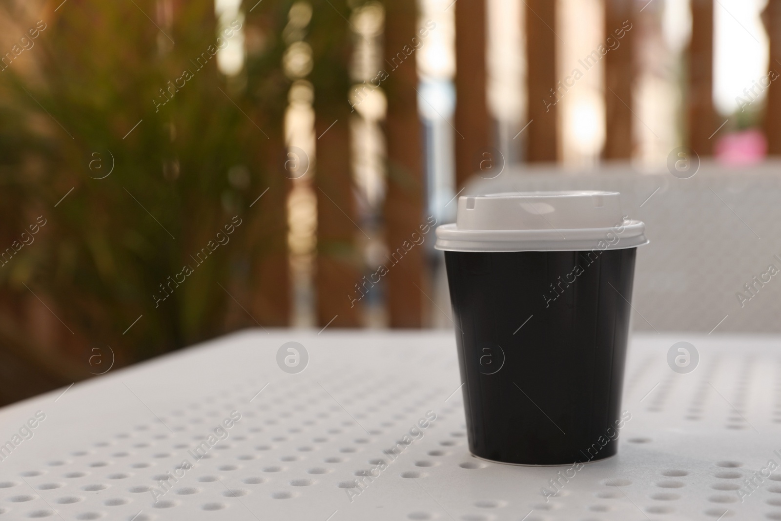 Photo of Takeaway paper cup with plastic lid on white table indoors, space for text