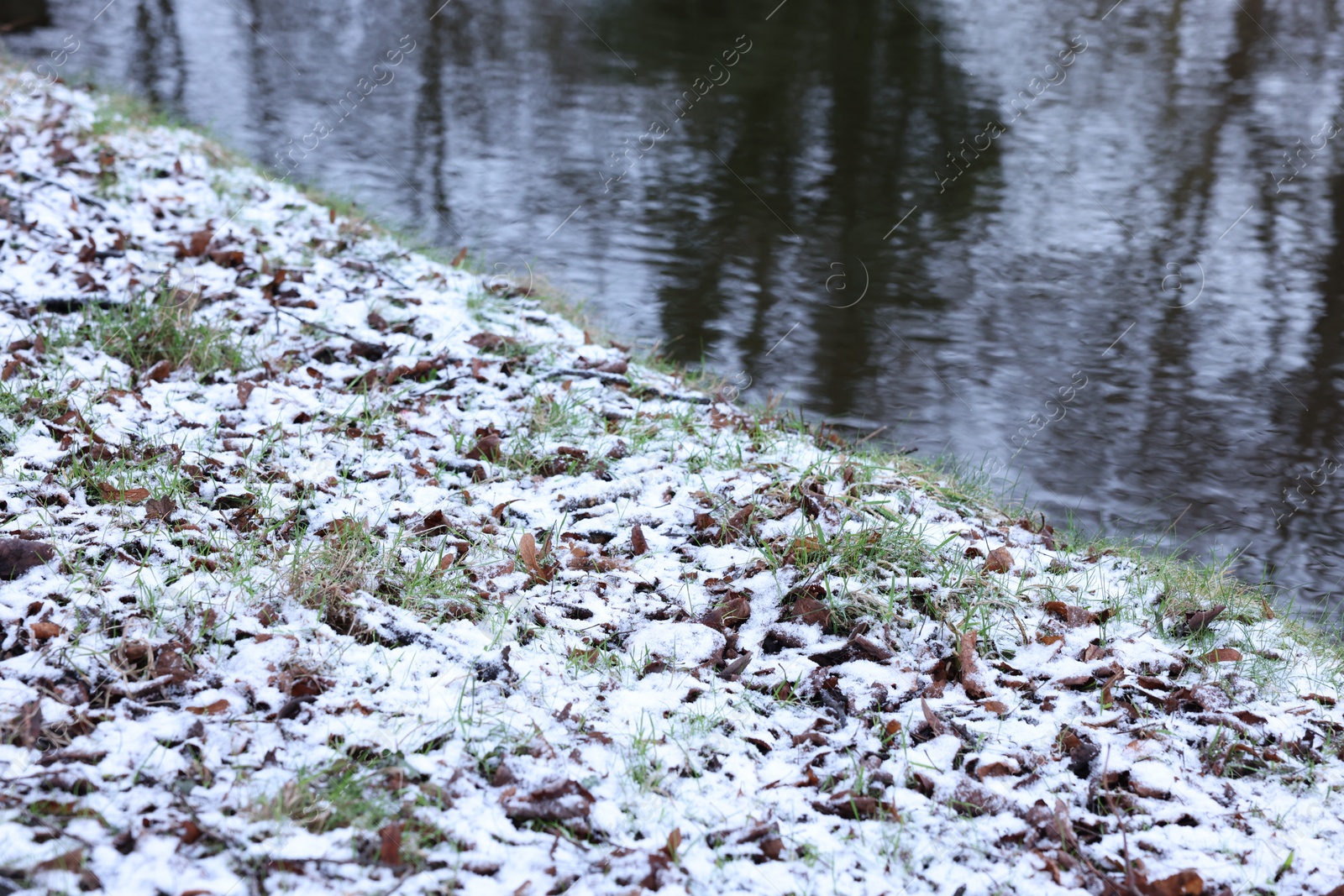 Photo of Green grass covered with snow and water canal on winter day