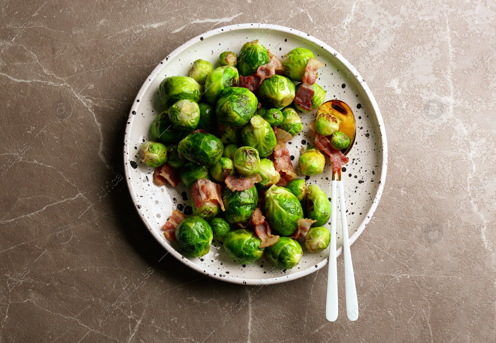 Photo of Delicious Brussels sprouts with bacon on marble table, top view