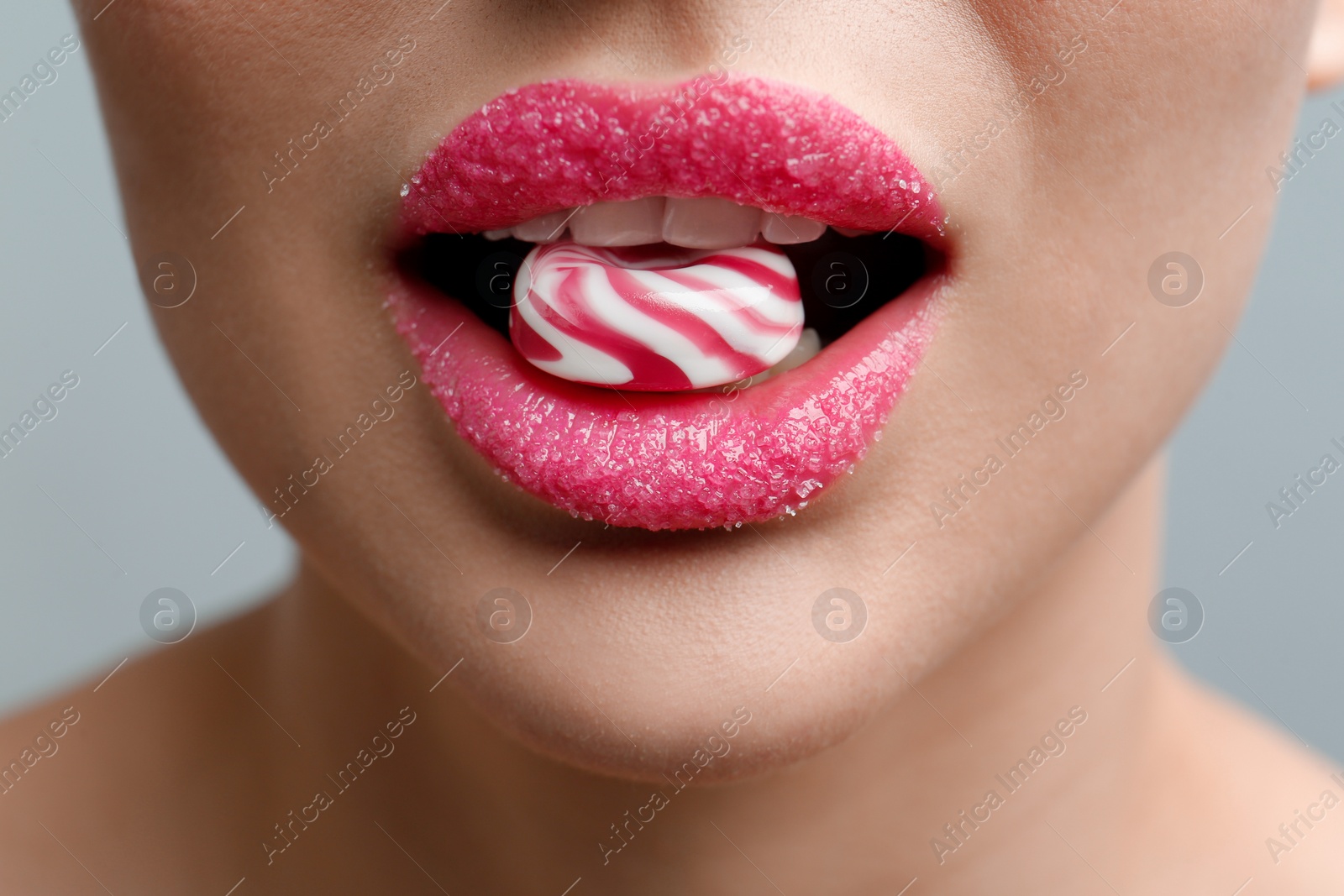 Photo of Woman with lips covered in sugar eating candy on light grey background, closeup