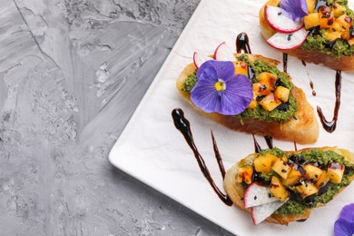 Photo of Delicious bruschettas with pesto sauce, tomatoes, balsamic vinegar and violet flower on gray textured table, top view. Space for text