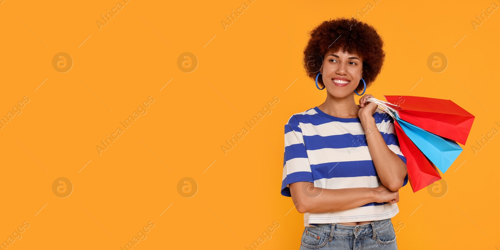 Photo of Happy young woman with shopping bags on orange background. Space for text