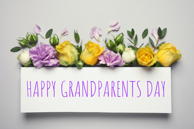 Flat lay composition with beautiful blooming flowers and phrase HAPPY GRANDPARENTS DAY on grey background