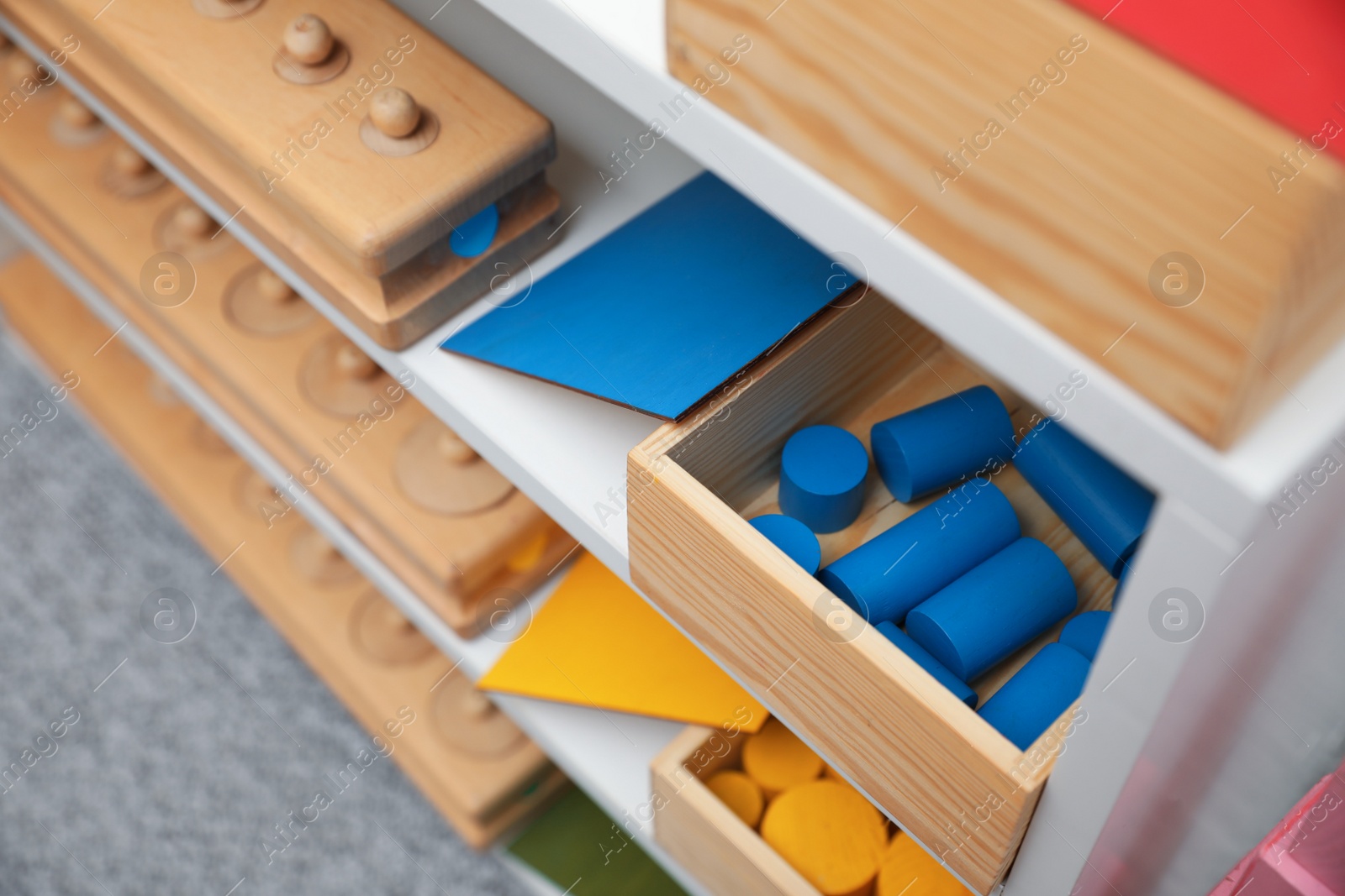 Photo of Set of wooden geometrical objects and other montessori toys on shelves, closeup