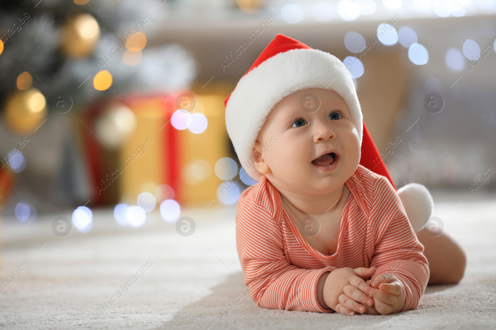 Photo of Little baby wearing Santa hat on floor indoors. First Christmas