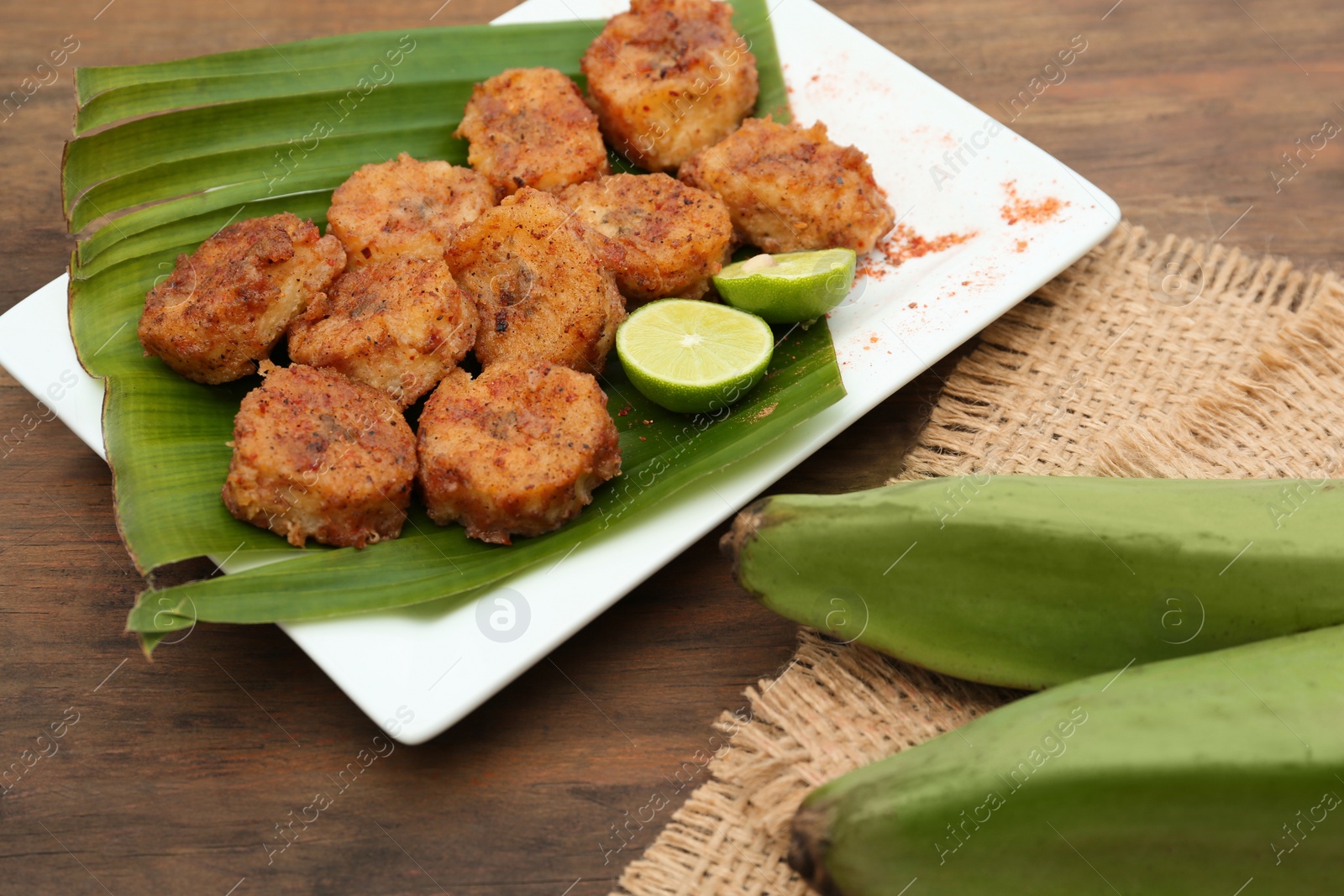 Photo of Delicious fried bananas, fresh fruits and cut limes on wooden table