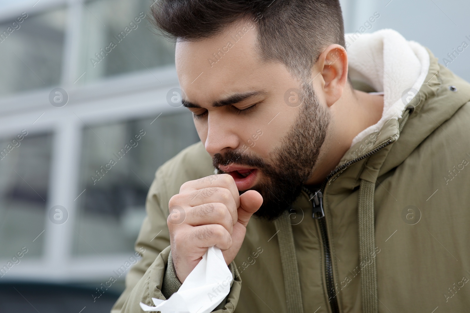 Photo of Sick man with tissue coughing outdoors. Cold symptoms