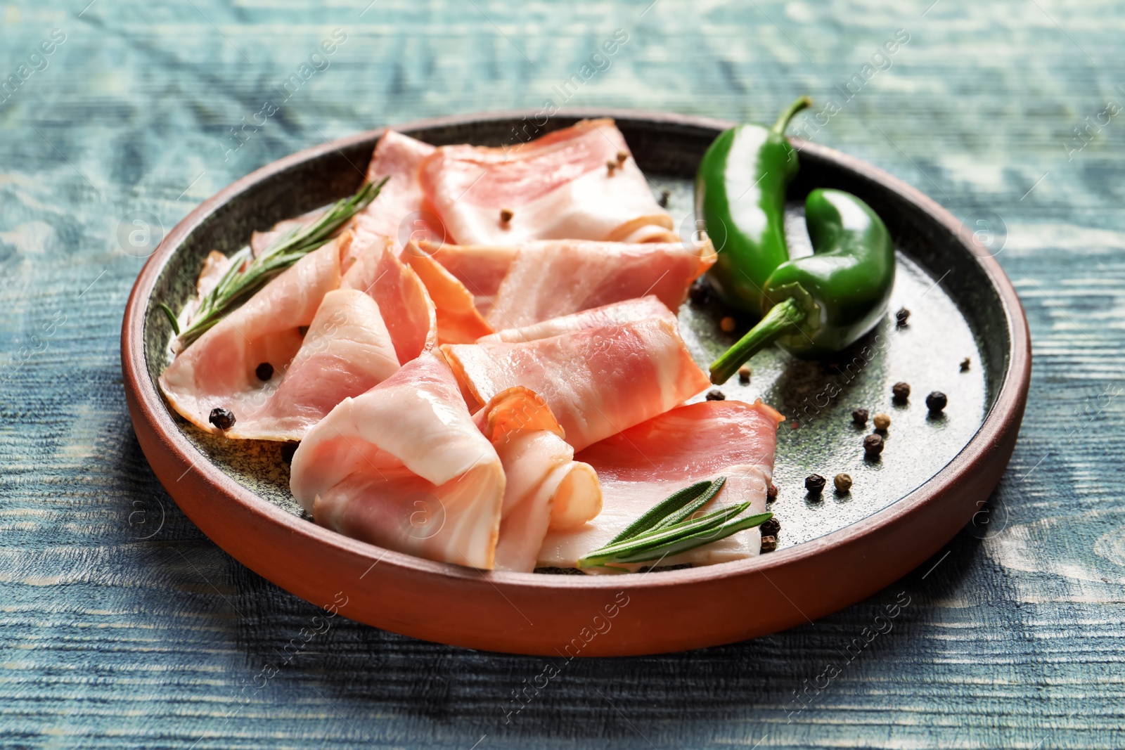 Photo of Plate with raw bacon rashers and peppers on wooden background