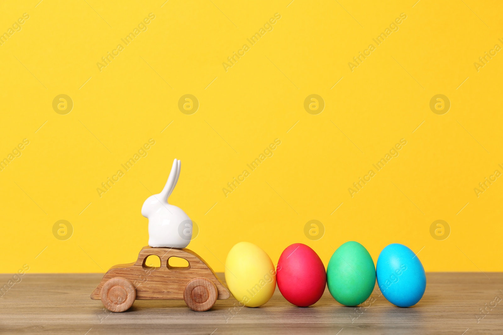 Photo of Toy car with ceramic bunny and Easter eggs on wooden table against color background