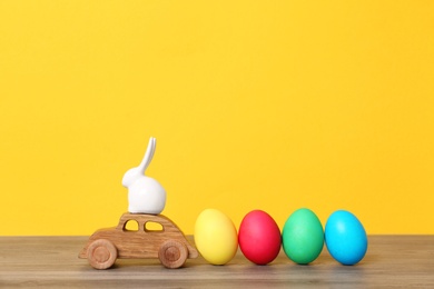 Photo of Toy car with ceramic bunny and Easter eggs on wooden table against color background