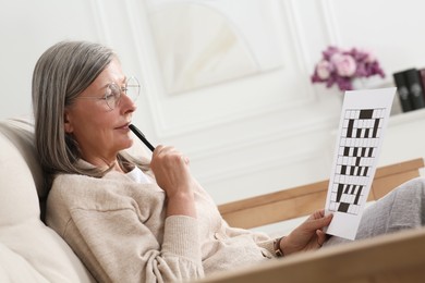 Photo of Senior woman solving crossword on sofa at home