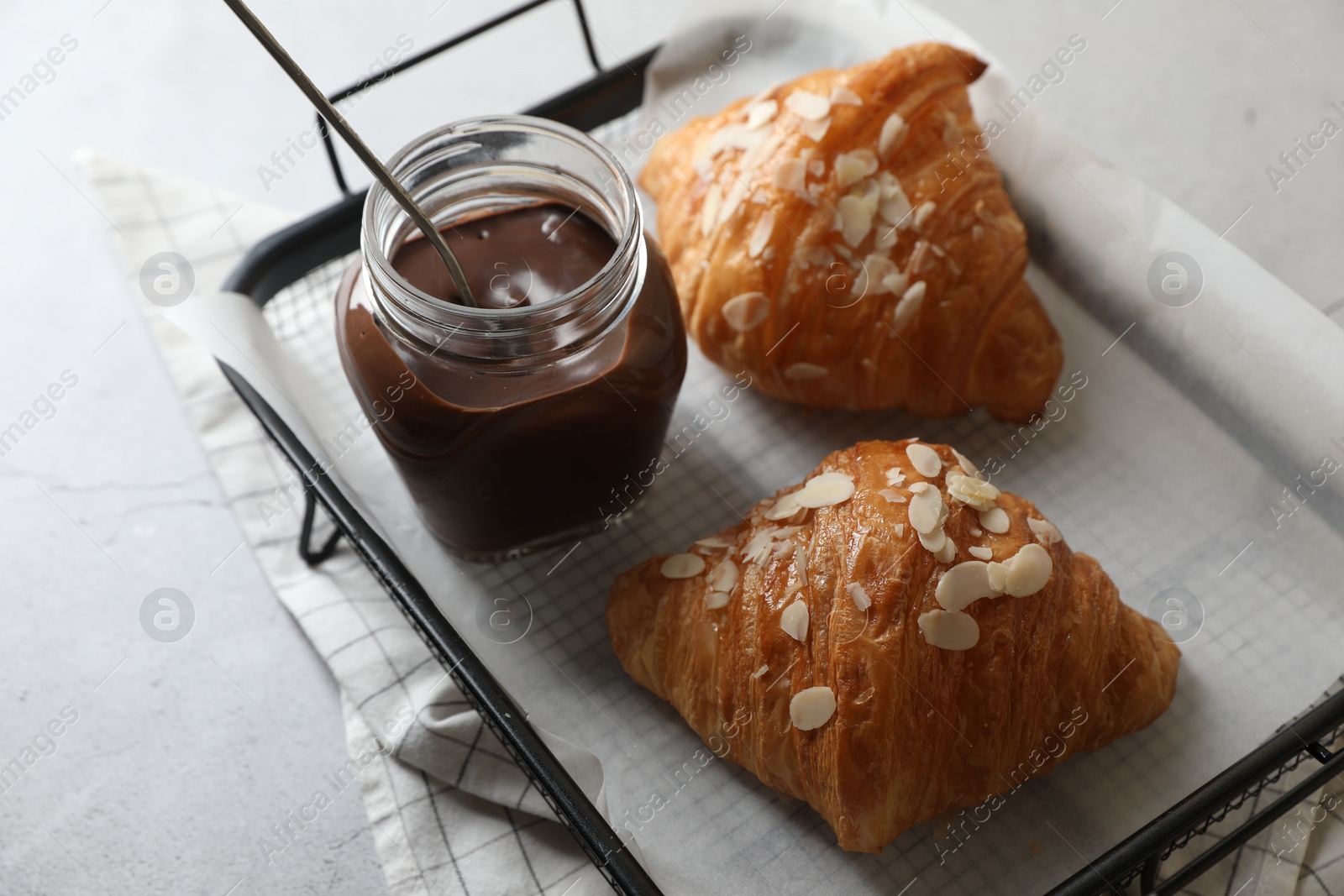 Photo of Delicious croissants with almond flakes and chocolate paste on light grey table, closeup