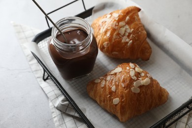 Delicious croissants with almond flakes and chocolate paste on light grey table, closeup