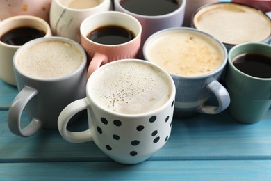 Photo of Many cups of different coffee drinks on light blue wooden table