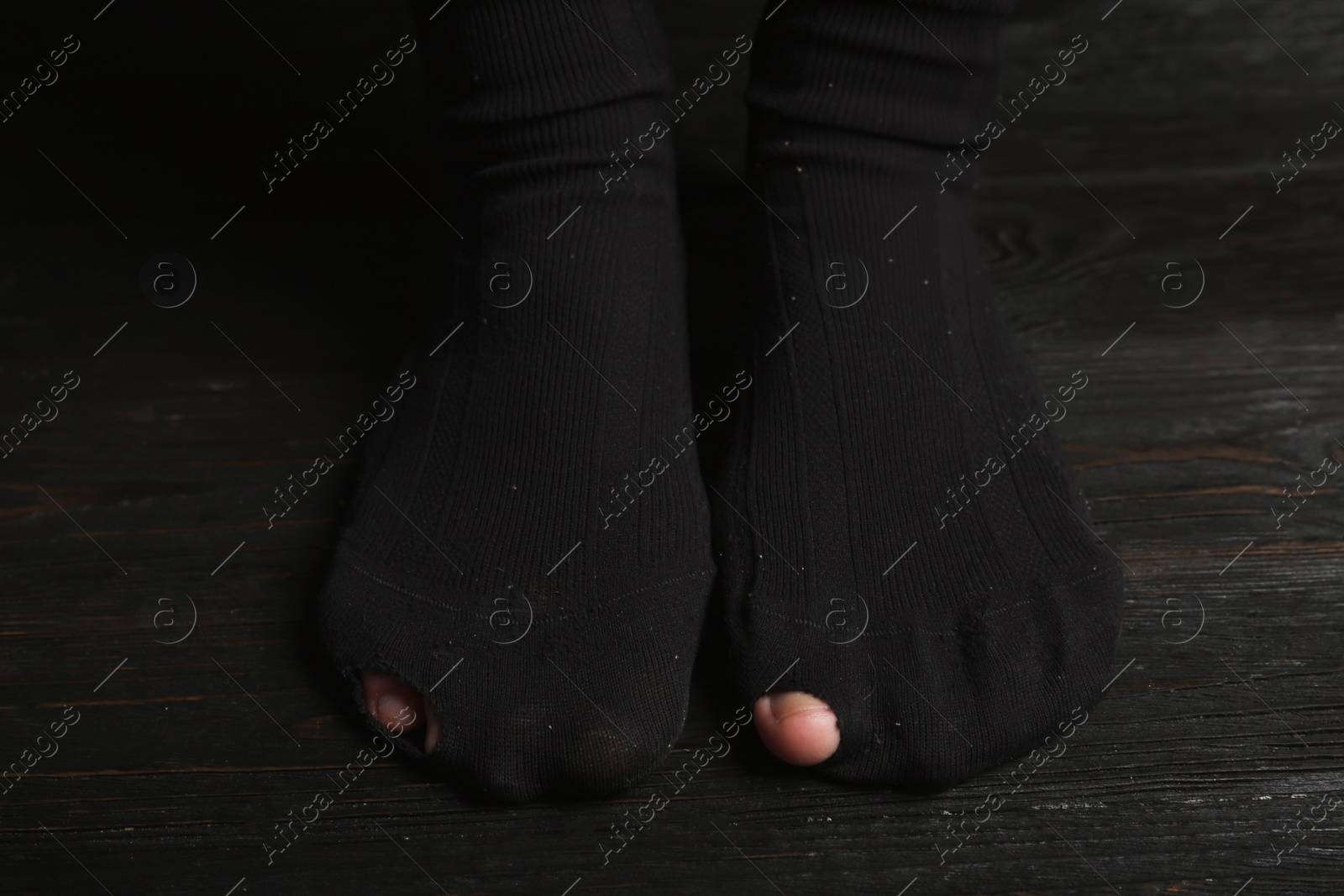 Photo of Poor person in shabby socks on wooden floor, closeup