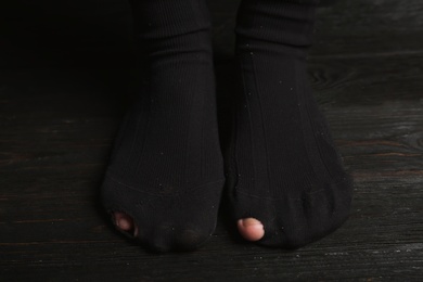 Photo of Poor person in shabby socks on wooden floor, closeup