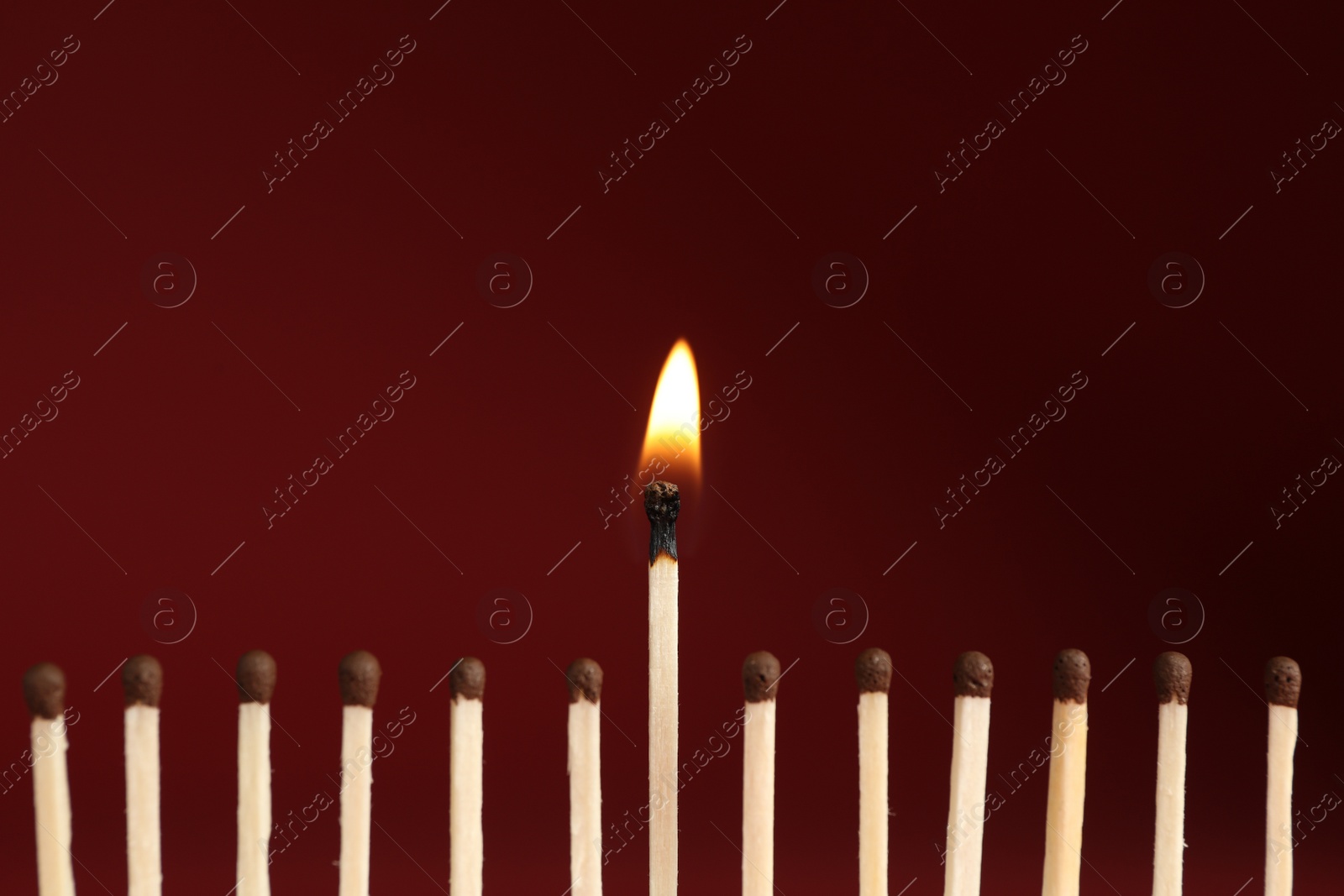 Photo of Burning match among unlit ones on red background, closeup