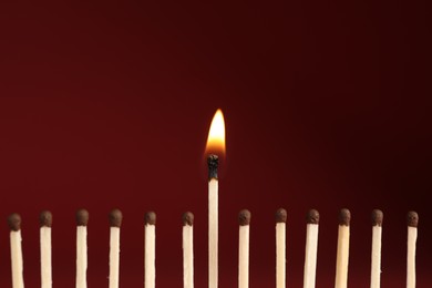 Photo of Burning match among unlit ones on red background, closeup