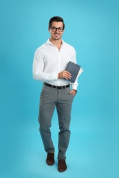 Photo of Young male teacher with glasses and notebooks on light blue background