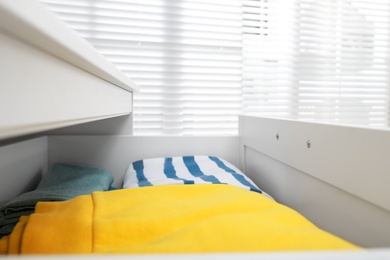 Modern open chest of drawers with clothes in room, closeup