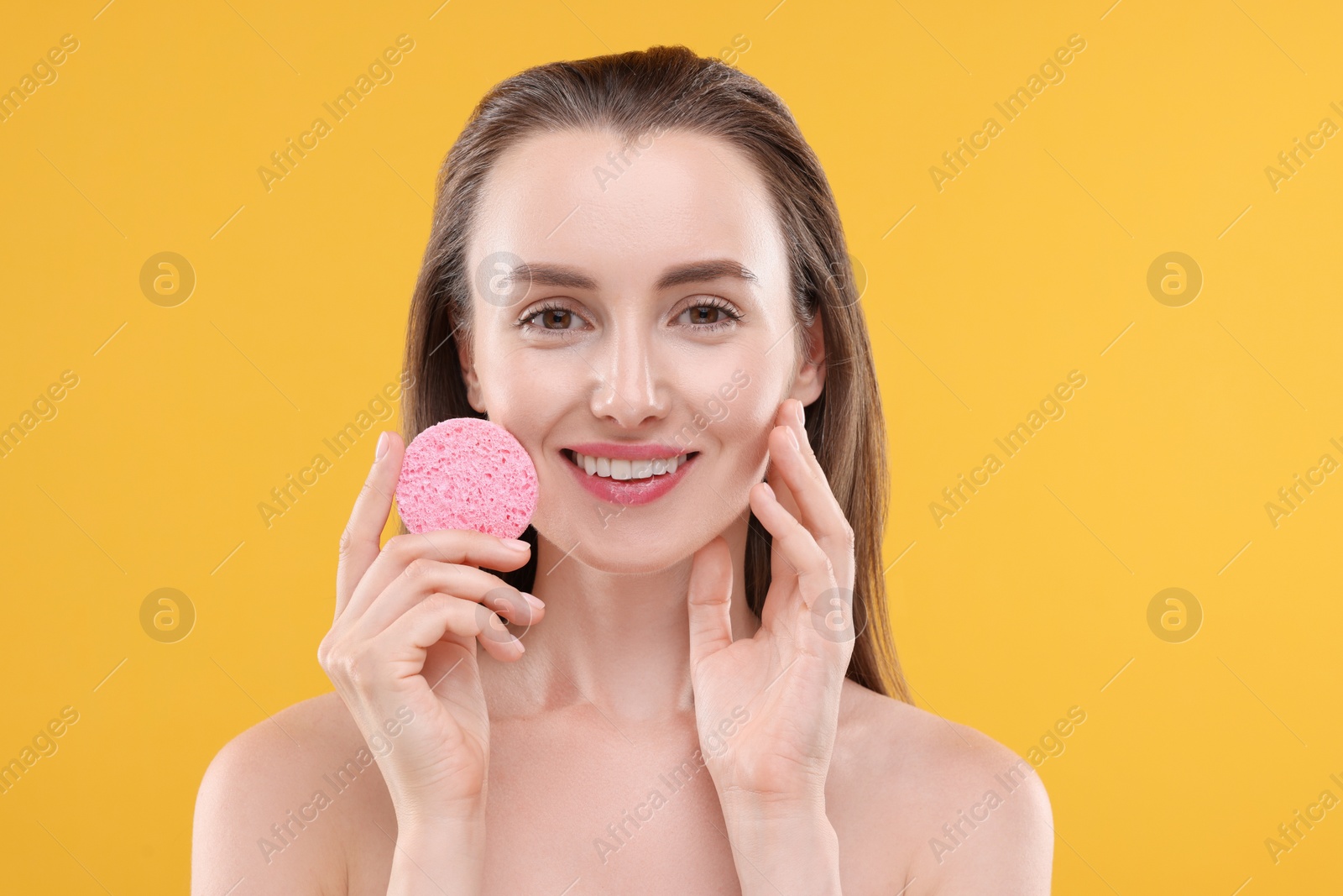 Photo of Happy young woman washing her face with sponge on orange background