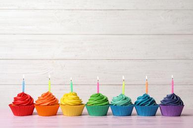 Delicious birthday cupcakes with burning candles on pink table