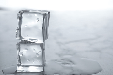 Photo of Wet ice cubes on white table, closeup. Space for text