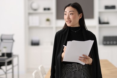 Portrait of smiling businesswoman with documents in office. Space for text